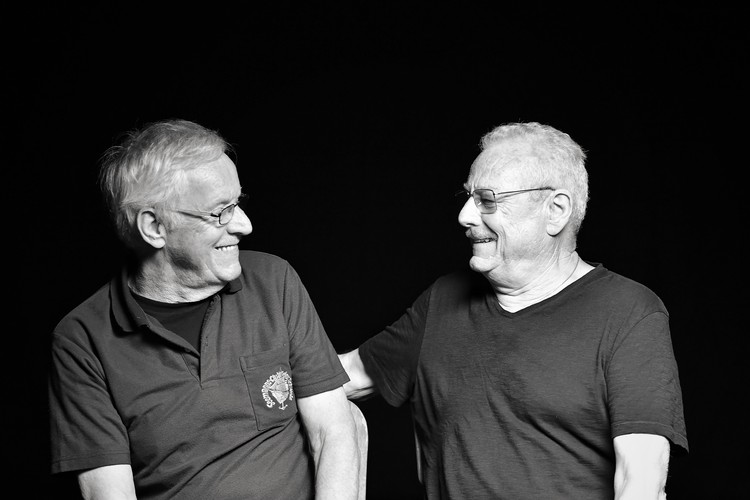 Black and white photo of the two brothers Peter und Kurt Bönzli. Sie sitzen einander zugewandt und lachen gemeinsam.